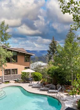 The image shows a scenic view of a pool area surrounded by trees and a mountain backdrop, creating a relaxing environment.