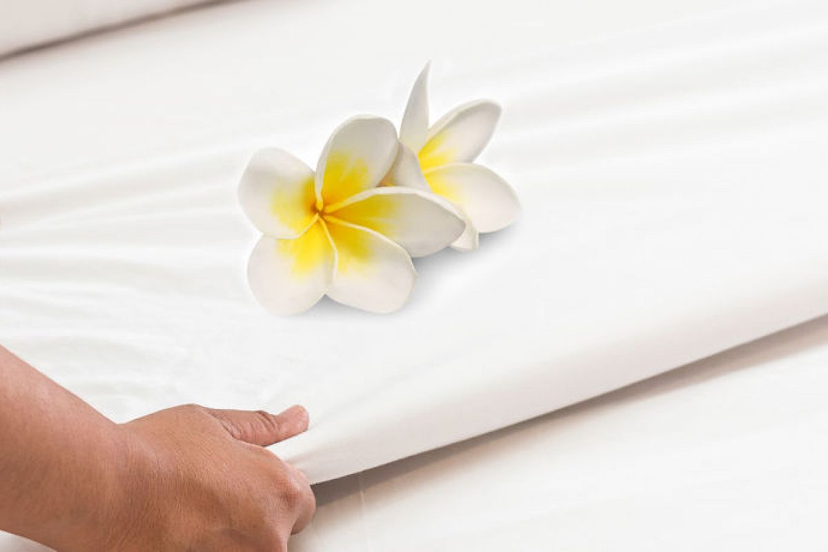 The image shows hands adjusting a white sheet or fabric with a pair of white and yellow flowers placed on top of it.