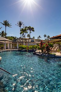 The image features a sunny pool area surrounded by palm trees, lounge chairs, umbrellas, and vibrant flowers. It's a tropical paradise.