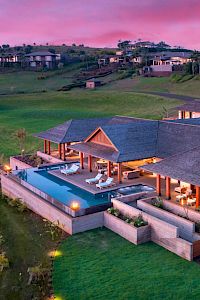 A luxurious villa with a pool, surrounded by lush greenery and hills under a vibrant sunset sky. It exudes elegance and tranquility.