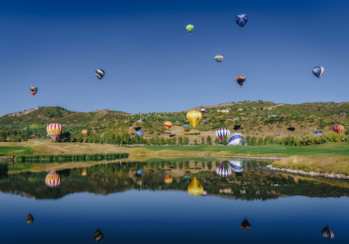 The image showcases colorful hot air balloons floating over a serene landscape, reflected in a calm body of water below.