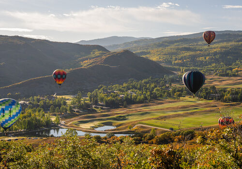The image showcases colorful hot air balloons floating over a scenic landscape of mountains and valleys with greenery.