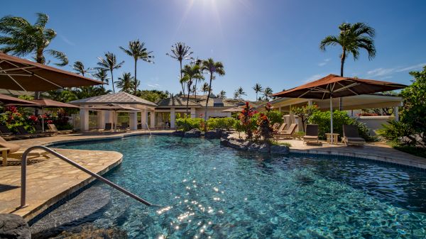 A sunny day at a resort with a swimming pool, surrounded by palm trees and lounging chairs under umbrellas, perfect for relaxation.