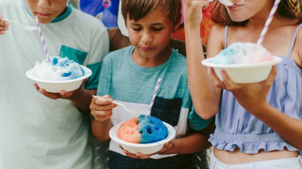 Kids enjoying colorful shaved ice with spoons and straws on a sunny day, each holding a bowl filled with sweet treats.