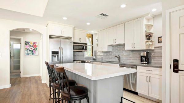 A modern kitchen with white cabinets, stainless steel appliances, and a center island with chairs is shown.