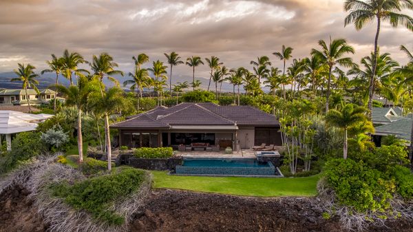 A luxury beachfront house with a pool, surrounded by lush greenery and palm trees, providing a scenic and tranquil setting.