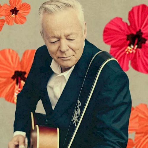 A person in a suit playing a guitar, with a background of bright red and orange flowers, creating a vibrant and artistic atmosphere.