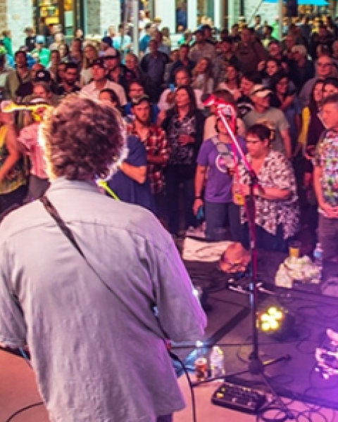 A band performs on stage to a large crowd at an outdoor event, with people enjoying the lively atmosphere.