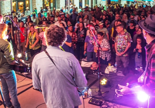 A band performs on stage to a large crowd at an outdoor event, with people enjoying the lively atmosphere.
