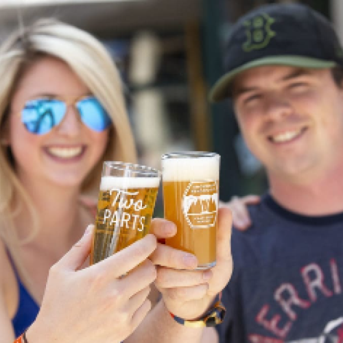 Two people are smiling and holding up glasses of beer for a cheers.