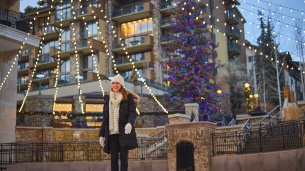 A person is ice skating in a festive outdoor setting with lights and a decorated tree in the background.