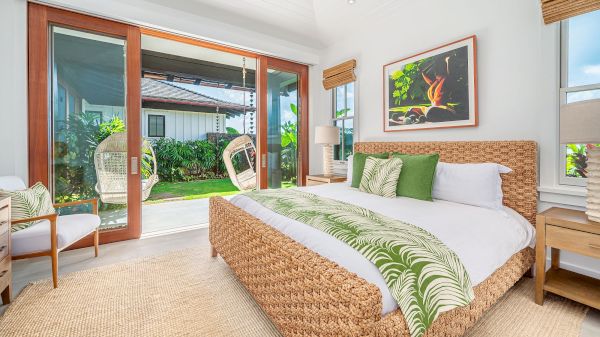 This image shows a bright bedroom with a woven bed, green accents, large sliding doors to a patio, and a peaceful, natural vibe.