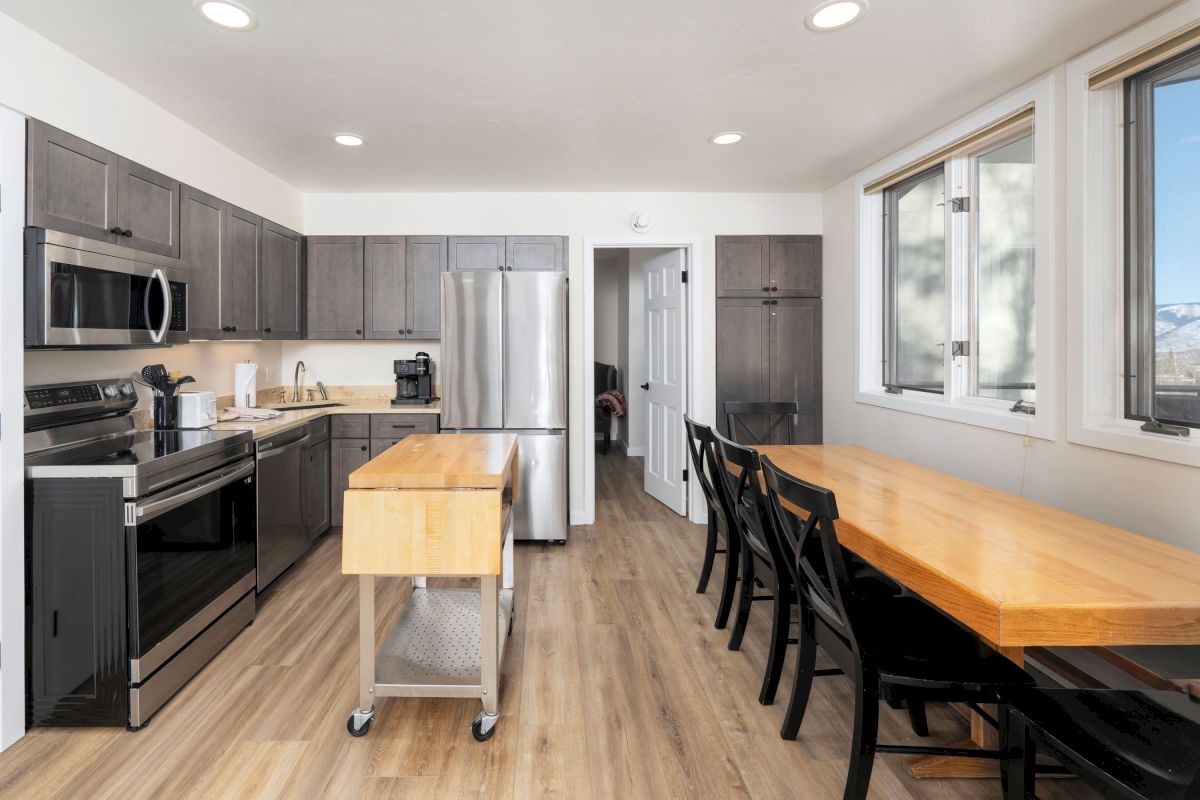 A modern kitchen with stainless steel appliances, a wooden island, and an adjacent dining area with a long table and black chairs.