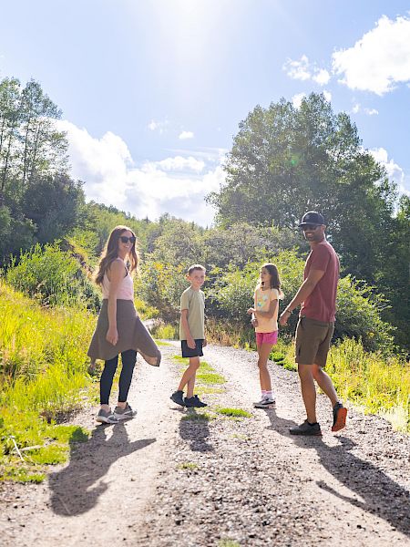 A group of people walking on a dirt path surrounded by lush greenery and mountains under a bright blue sky with fluffy clouds.