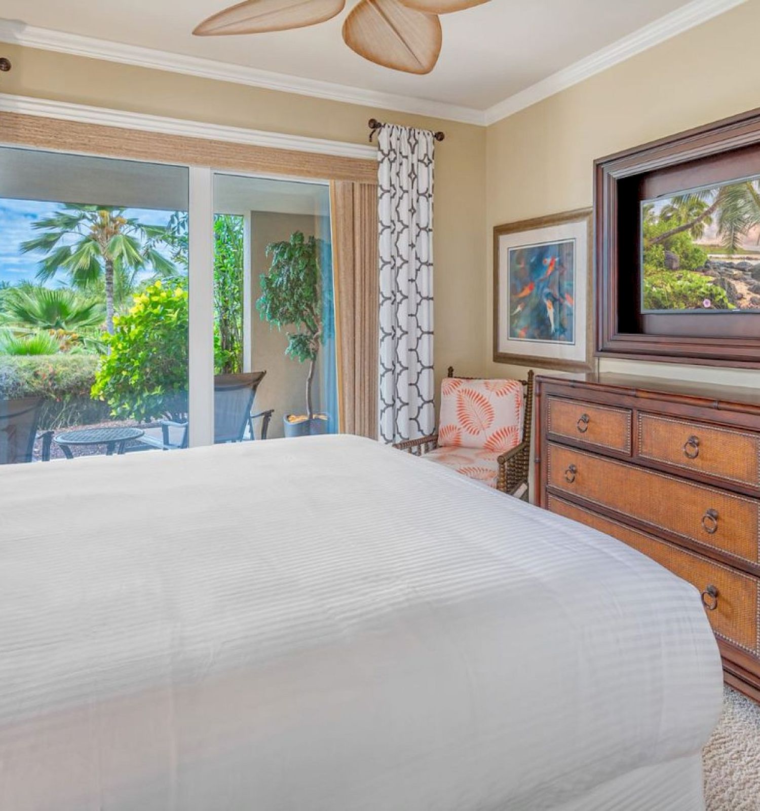 A cozy bedroom with a large bed, dresser, and window offers a view of a lush garden, and there’s artwork on the walls.