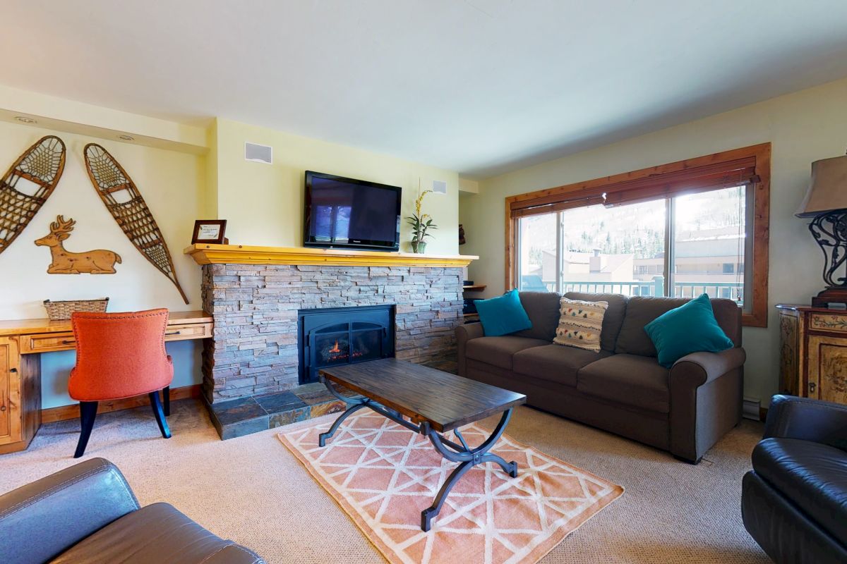 A cozy living room with a sofa, armchairs, TV, fireplace, desk, and snowshoe wall decor.