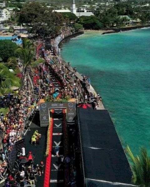 Aerial view of a coastal marathon event with crowds, a red finish line, and turquoise ocean on a sunny day.