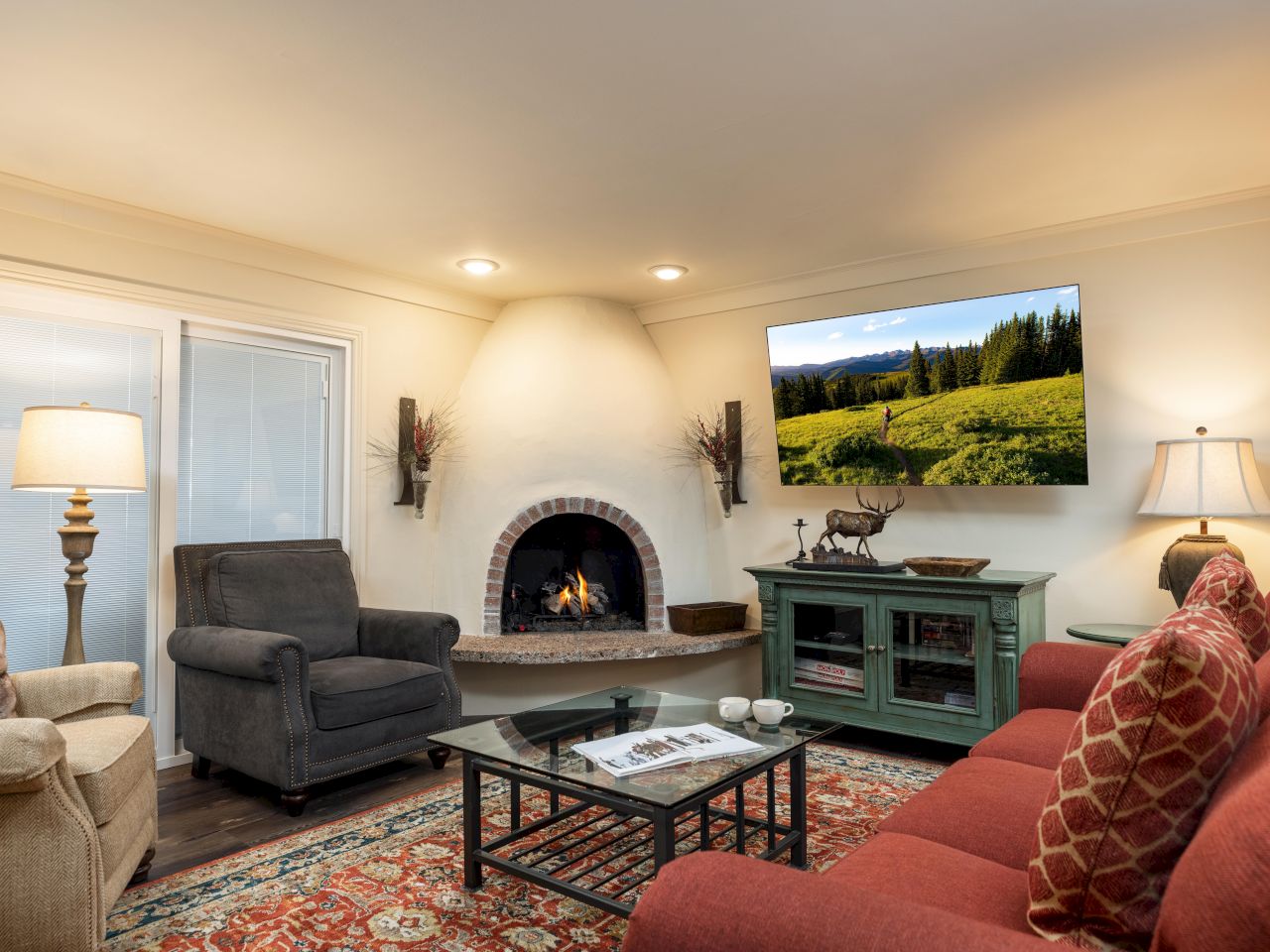 A cozy living room with a fireplace, couch, armchairs, TV, lamps, and a rug, creating a warm and inviting atmosphere.