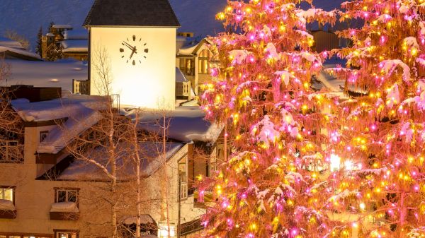 The image features a snowy scene with illuminated Christmas trees, a clock tower, and charming buildings, creating a festive atmosphere.
