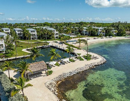 The image shows a tropical beach area with white buildings, palm trees, and clear water. It's a serene getaway spot.