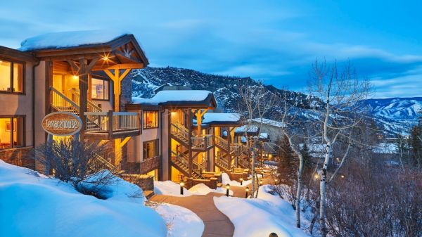 The image shows a cozy, snow-covered lodge called "Terracehouse" surrounded by mountain scenery and evening lights.