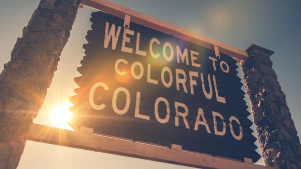 A sign that reads "Welcome to Colorful Colorado," with a bright sun shining behind it. The scene is warm and inviting.
