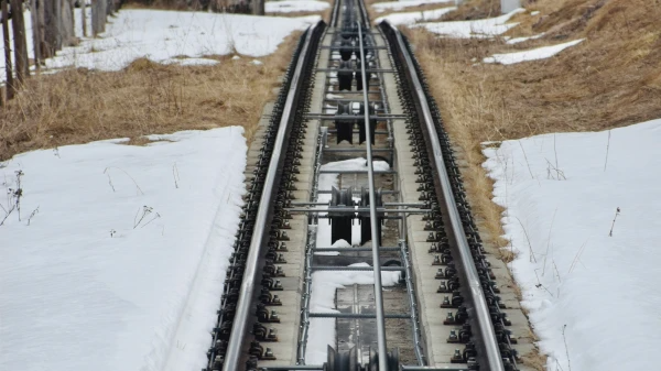 The image shows a railway track with patches of snow and brown grass, leading into the distance. It's a quiet, winter scene.