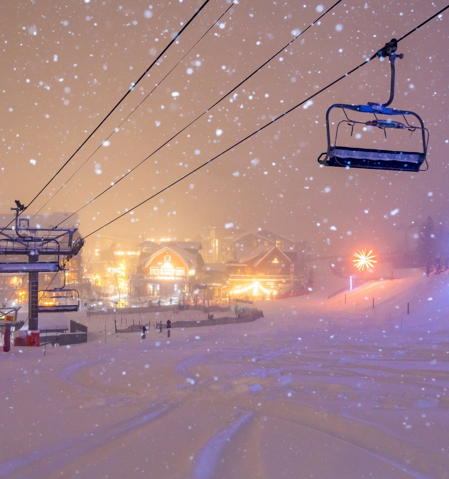 A snowy scene features a ski lift above a winter resort, glowing lights, and soft flurries falling in the tranquil atmosphere.