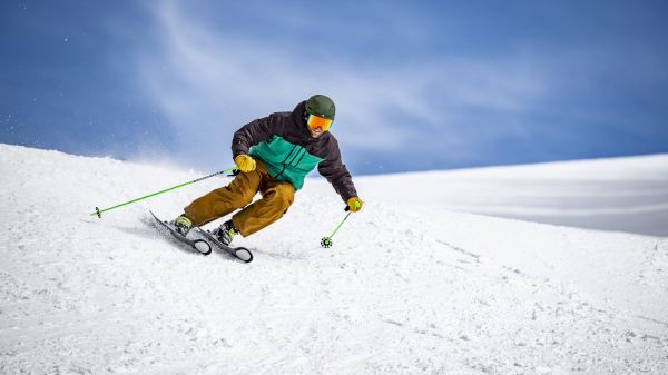 A skier in colorful gear expertly navigates a snowy slope against a clear blue sky, showcasing winter sports excitement.