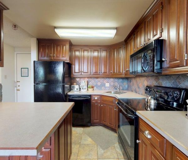 The image shows a kitchen with wooden cabinets, black appliances, and a tiled backsplash, creating a warm and inviting space.