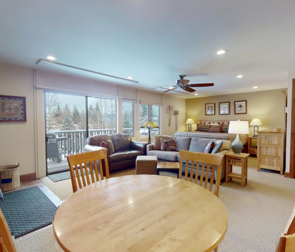 The image features a cozy living area with a stone fireplace, wooden furniture, and large windows showing a snowy landscape outside.