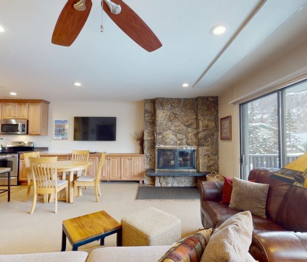 The image shows a cozy living area with a kitchen, dining table, and a stone fireplace, creating a warm ambiance.