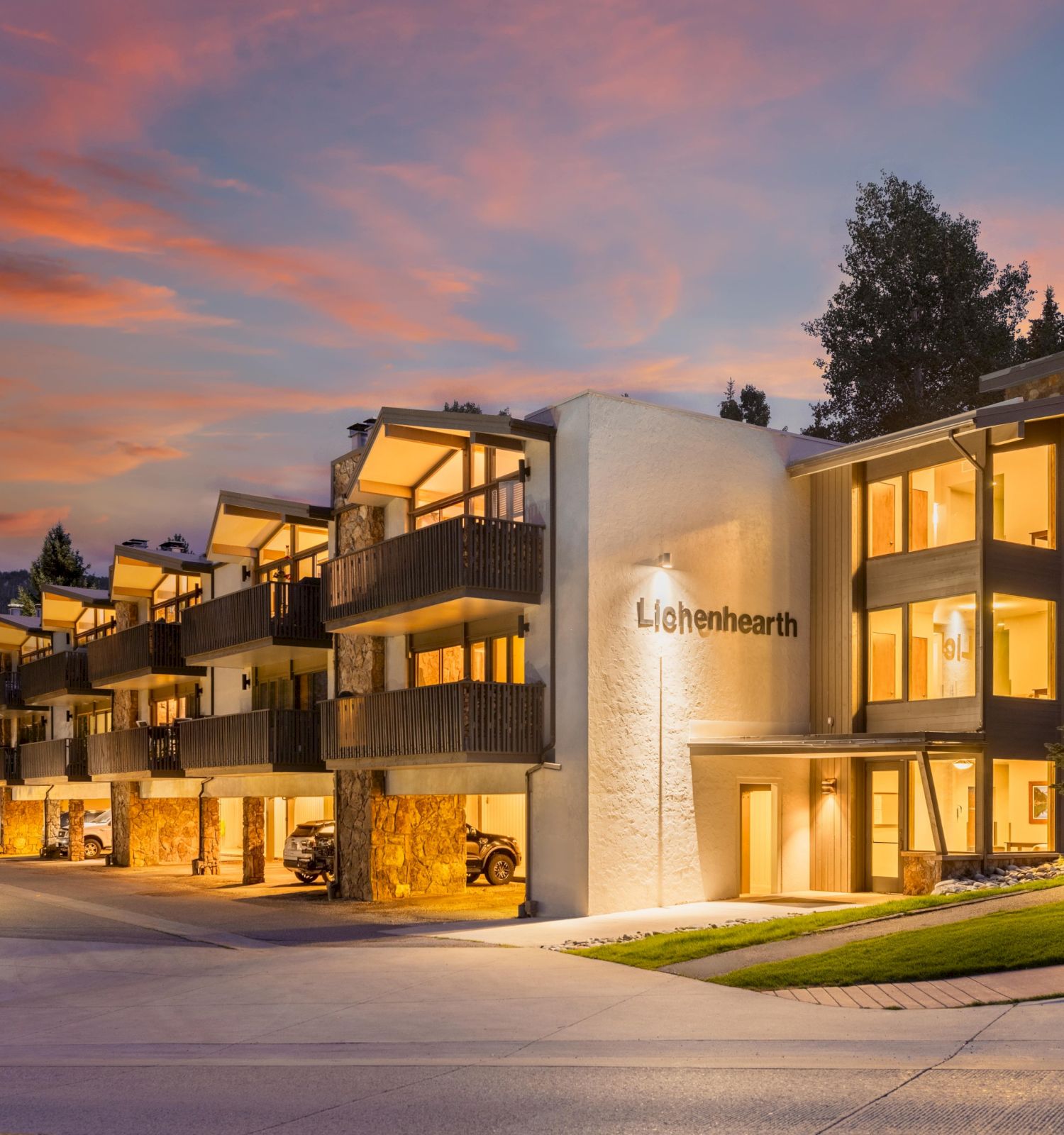 The image shows a modern building named Lichenhearth, illuminated at dusk with trees and a colorful sky in the background.