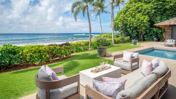 A tranquil outdoor space with soft seating, a pool, and beautiful ocean views framed by palm trees and lush greenery.