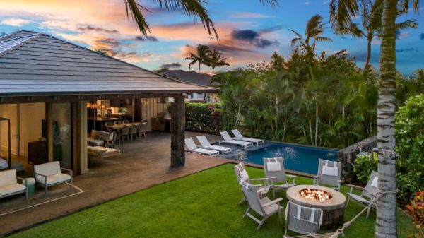 A serene backyard features a pool, fire pit, and lounge chairs, set against a colorful sunset sky and lush greenery.