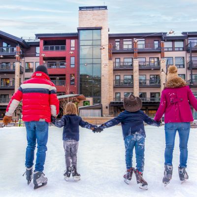 A family skates together on an ice rink in front of a cozy lodge, creating joyful winter memories. The scene is lively and cheerful.