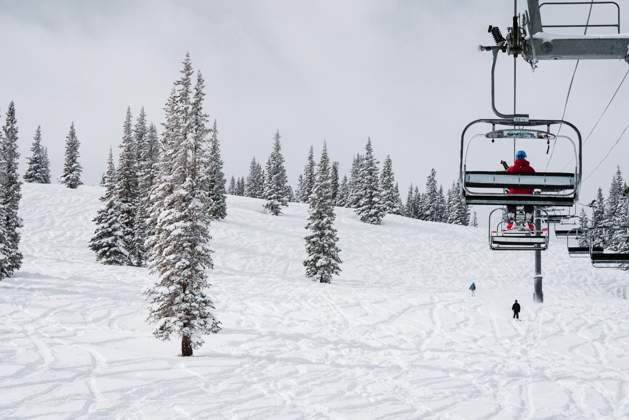 The image shows a snowy ski resort with a ski lift, trees, and skiers enjoying the slopes in a winter landscape.