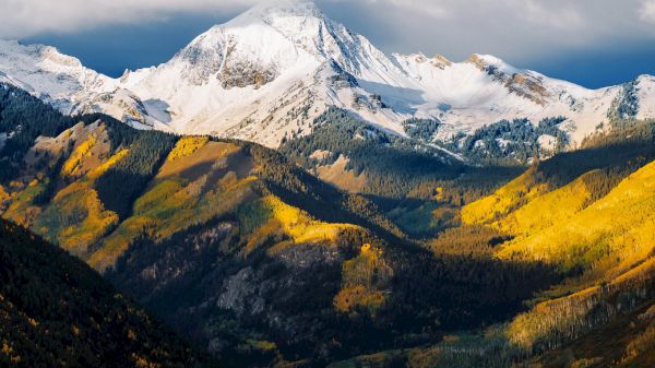 The image showcases majestic snow-capped mountains with vibrant autumn foliage below, creating a stunning natural landscape.