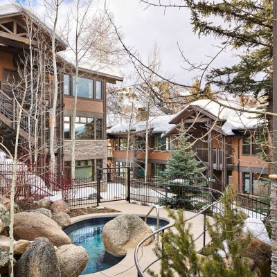 The image features a scenic courtyard with stone landscaping, a small pool, and modern buildings surrounded by trees and snow.