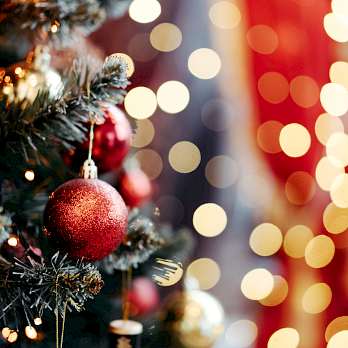 A decorated Christmas tree with red baubles and warm, blurred holiday lights in the background.