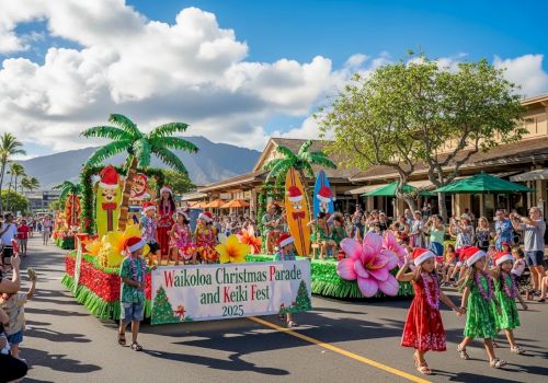 A festive parade on a sunny street with colorful floats, tropical palm props, dancers in bright skirts, and a banner reading “Wailoa Christmas Parade and Keki Fest” amid cheering crowds.