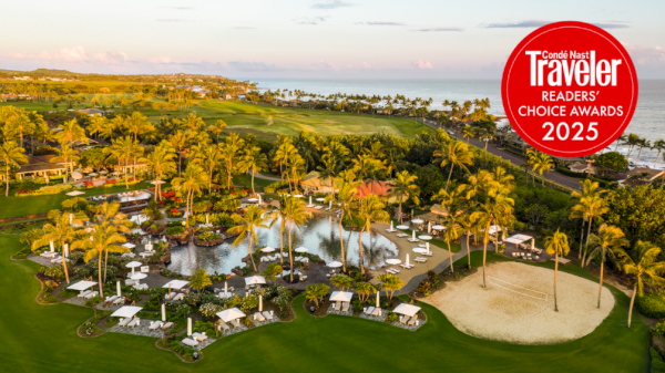 A tropical resort with palm trees, a pool, lounge chairs, and a sandy beach area near the ocean, plus a red travel award badge in the top-right corner.