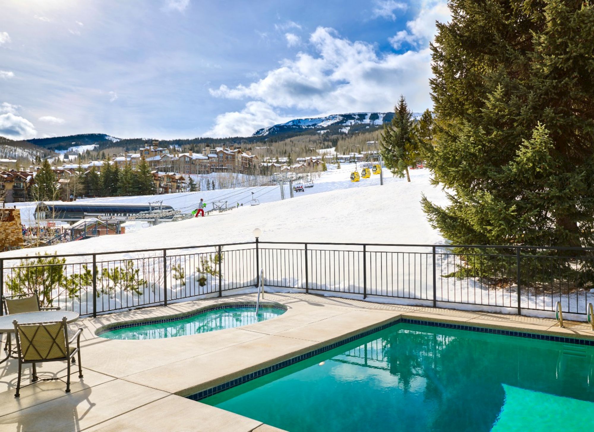 The image shows a winter landscape with ski slopes, a hot tub, and snowy mountains under a partly cloudy sky. It's a serene retreat.