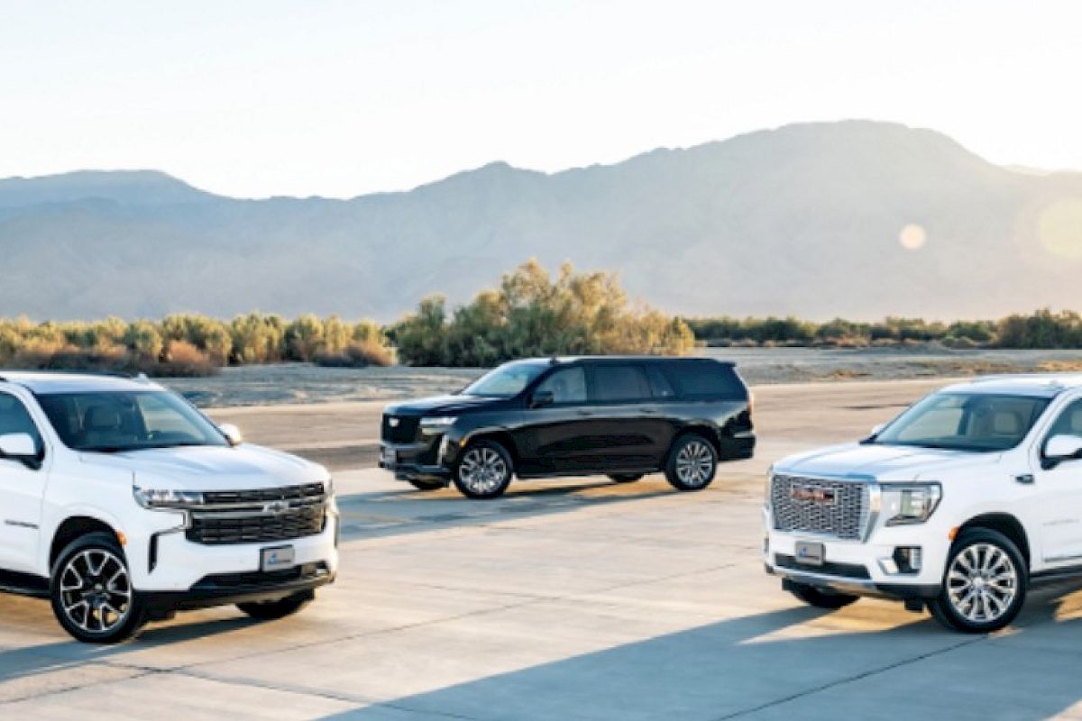 Three modern SUVs parked on a sunny tarmac with mountains in the distance.