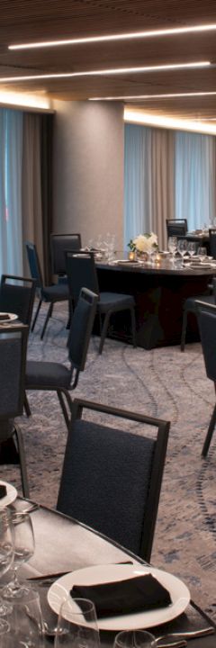 A decorated banquet hall with round tables set with plates, glasses, and silverware, and chairs arranged around them.